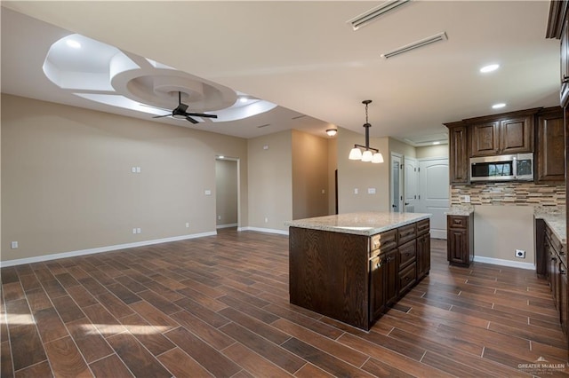 kitchen featuring dark brown cabinetry, stainless steel microwave, wood finish floors, backsplash, and ceiling fan with notable chandelier