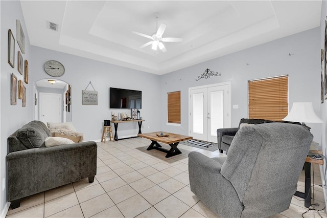 living area featuring arched walkways, french doors, a tray ceiling, and light tile patterned flooring