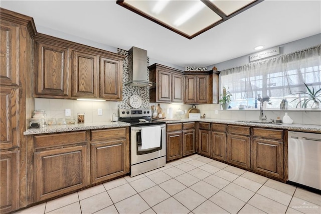 kitchen with tasteful backsplash, appliances with stainless steel finishes, a sink, wall chimney range hood, and light stone countertops