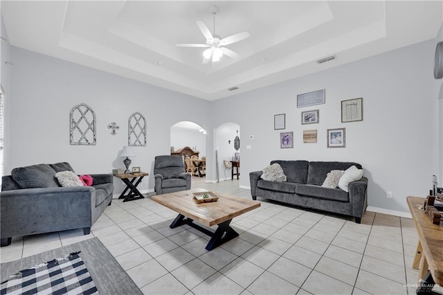 living room featuring arched walkways, light tile patterned flooring, visible vents, baseboards, and a raised ceiling