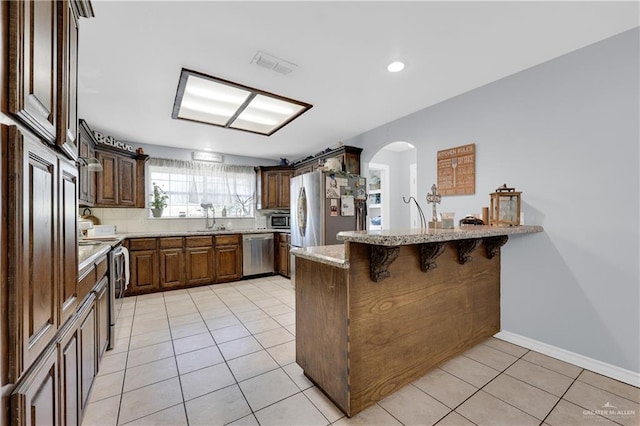 kitchen featuring a peninsula, appliances with stainless steel finishes, a kitchen bar, and visible vents