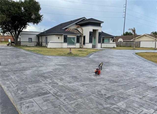 view of front of property featuring central air condition unit, fence, decorative driveway, stucco siding, and a front lawn