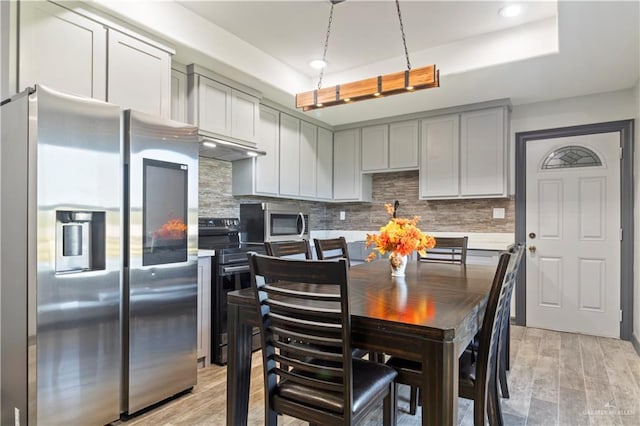 kitchen featuring appliances with stainless steel finishes, tasteful backsplash, gray cabinetry, light hardwood / wood-style floors, and a tray ceiling