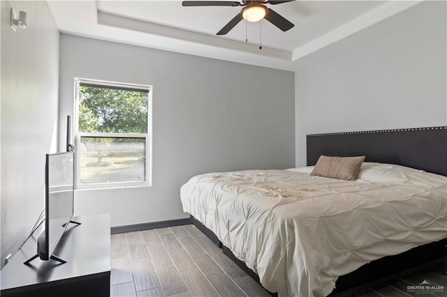 bedroom featuring hardwood / wood-style flooring, a raised ceiling, and ceiling fan