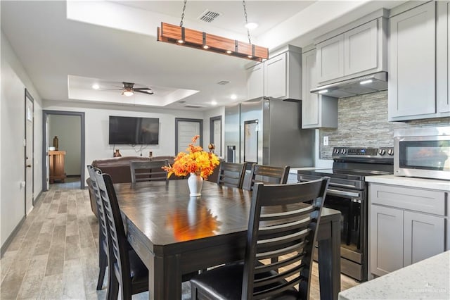 dining space featuring light hardwood / wood-style flooring, a raised ceiling, and ceiling fan