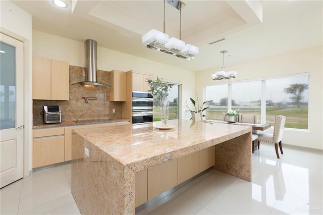 kitchen with light stone countertops, a center island, wall chimney exhaust hood, double oven, and pendant lighting