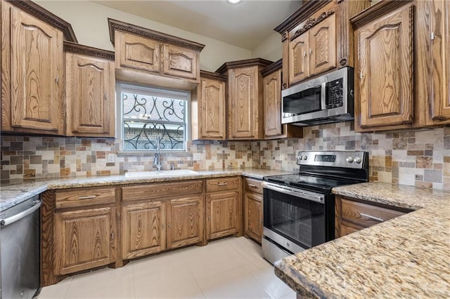 kitchen with appliances with stainless steel finishes, sink, backsplash, light tile patterned floors, and light stone countertops