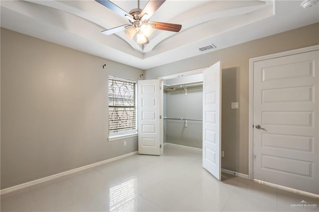 unfurnished bedroom with light tile patterned floors, a tray ceiling, a closet, and ceiling fan