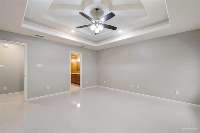 unfurnished bedroom with a raised ceiling, ensuite bathroom, light tile patterned flooring, and ceiling fan