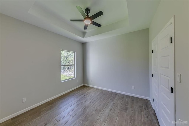 unfurnished room with ceiling fan, light wood-type flooring, and a tray ceiling