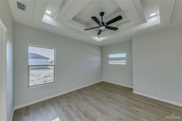 empty room featuring a tray ceiling, ceiling fan, and light wood-type flooring