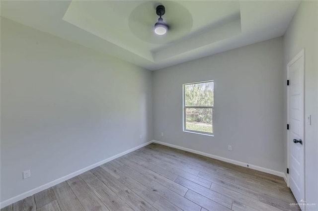 empty room with light hardwood / wood-style flooring, ceiling fan, and a tray ceiling