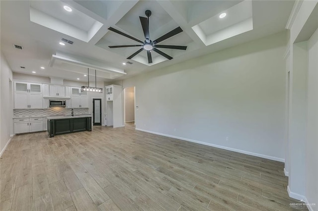 unfurnished living room featuring coffered ceiling, beam ceiling, ceiling fan, and light wood-type flooring