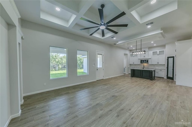 unfurnished living room with ceiling fan, beam ceiling, a high ceiling, coffered ceiling, and light hardwood / wood-style floors