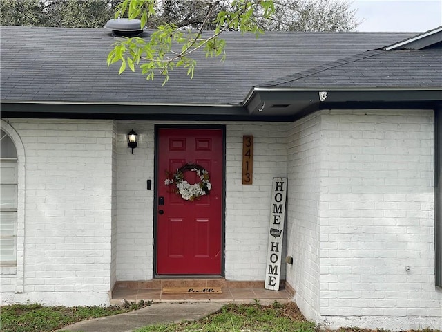 view of exterior entry featuring roof with shingles and brick siding