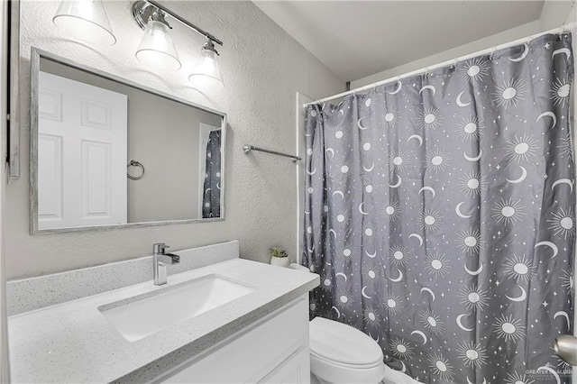 bathroom with a textured wall, vanity, toilet, and a shower with curtain