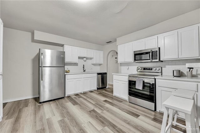 kitchen with arched walkways, light countertops, light wood-style flooring, decorative backsplash, and appliances with stainless steel finishes