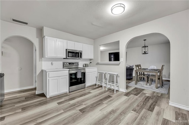 kitchen with arched walkways, light countertops, visible vents, appliances with stainless steel finishes, and white cabinetry