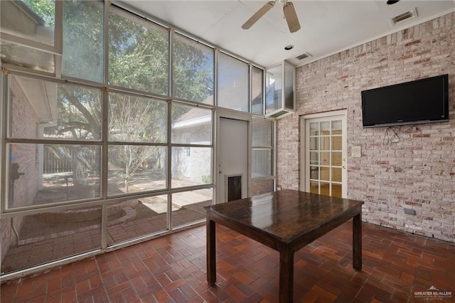 unfurnished office with brick floor, floor to ceiling windows, visible vents, ceiling fan, and brick wall