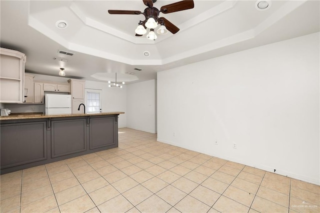 kitchen with sink, a tray ceiling, kitchen peninsula, white fridge, and ceiling fan