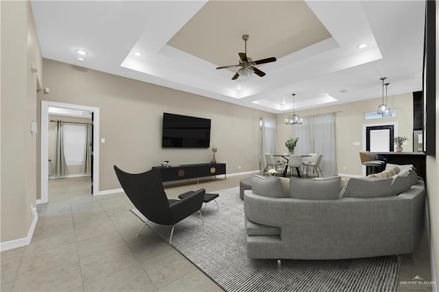 tiled living room with ceiling fan and a tray ceiling