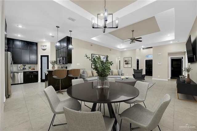 tiled dining room featuring ceiling fan with notable chandelier and a tray ceiling