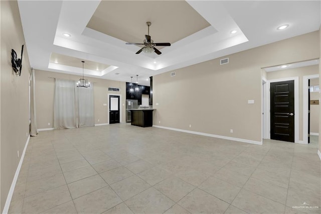 unfurnished living room with a raised ceiling, ceiling fan with notable chandelier, and light tile patterned floors