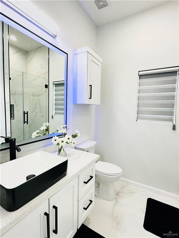 1509 Giselle St, Mission, TX 78574 - full bath featuring marble look tile flooring, a marble finish shower, baseboards, toilet, and vanity