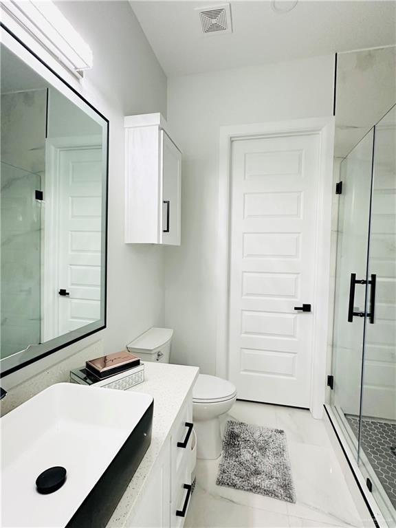 1509 Giselle St, Mission, TX 78574 - bathroom featuring marble look tiles, a stall shower, vanity, and toilet
