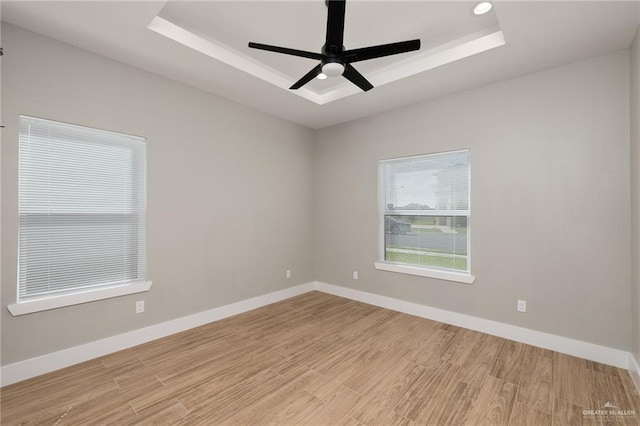 unfurnished room with baseboards, a raised ceiling, and light wood-style floors