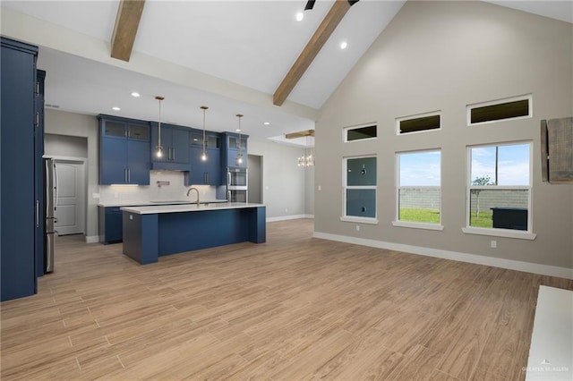 kitchen featuring a center island with sink, blue cabinets, light countertops, light wood-style floors, and beam ceiling