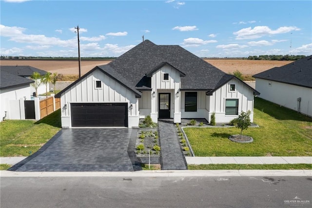 modern farmhouse with decorative driveway, an attached garage, board and batten siding, a front yard, and fence