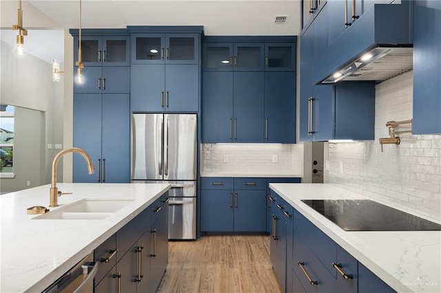 kitchen featuring appliances with stainless steel finishes, blue cabinets, a sink, and exhaust hood