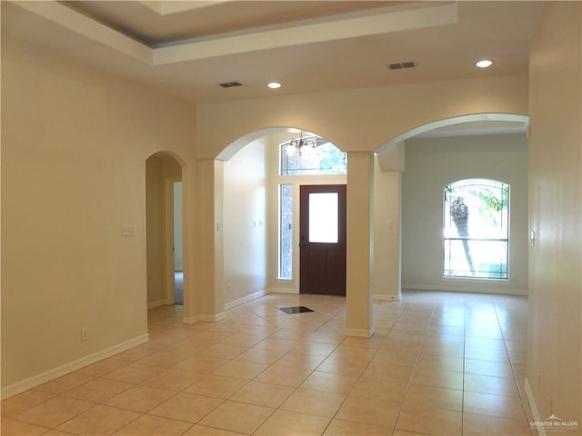 tiled entryway with a tray ceiling and an inviting chandelier