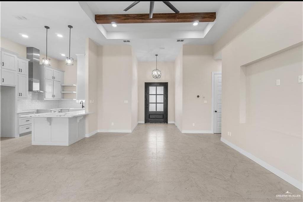 kitchen featuring hanging light fixtures, beamed ceiling, white cabinets, and wall chimney exhaust hood