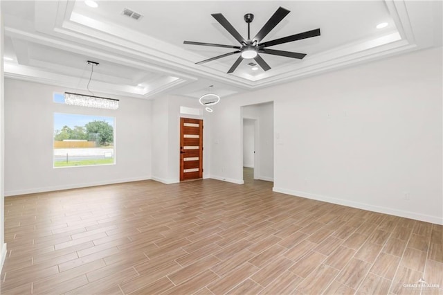 empty room featuring a raised ceiling, ceiling fan, and light hardwood / wood-style floors