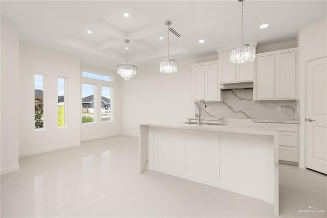 kitchen featuring white cabinetry, sink, light stone countertops, tasteful backsplash, and an island with sink