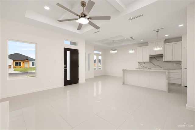 unfurnished living room with light tile patterned floors, a tray ceiling, and a healthy amount of sunlight