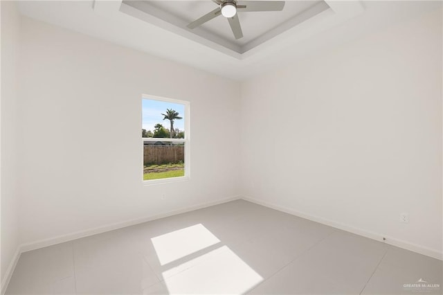 tiled empty room featuring a tray ceiling and ceiling fan