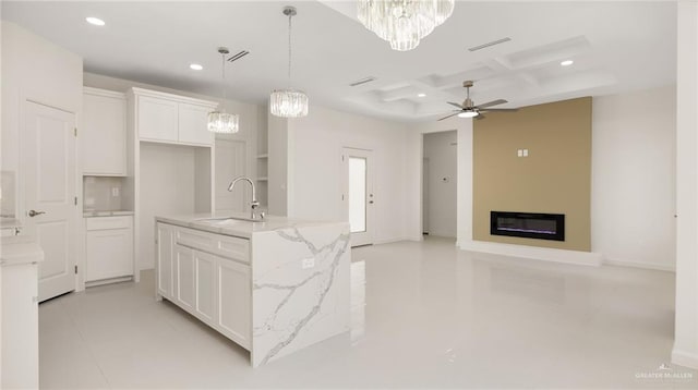 kitchen with light stone counters, ceiling fan, a kitchen island with sink, sink, and white cabinetry