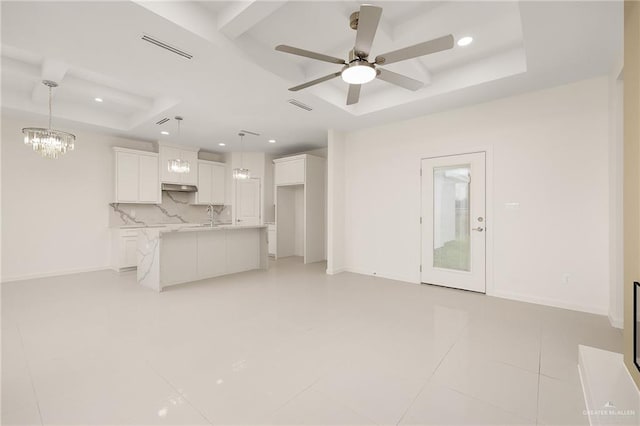 unfurnished living room featuring light tile patterned floors, ceiling fan with notable chandelier, a raised ceiling, and sink