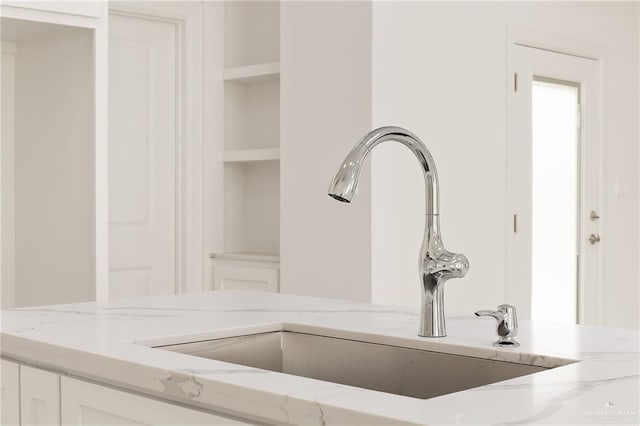 interior details with white cabinets, light stone counters, and sink