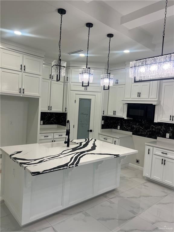 kitchen with a center island with sink, white cabinets, and decorative light fixtures