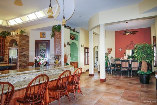 kitchen featuring a breakfast bar, stainless steel fridge with ice dispenser, light stone counters, and ceiling fan