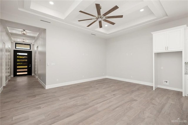 empty room featuring light wood-type flooring, a raised ceiling, and ceiling fan