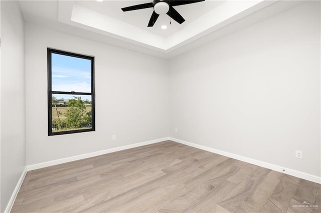 unfurnished room with ceiling fan, a raised ceiling, and light hardwood / wood-style flooring