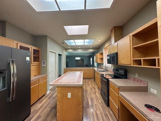 kitchen featuring sink, wood-type flooring, a skylight, a center island, and black appliances