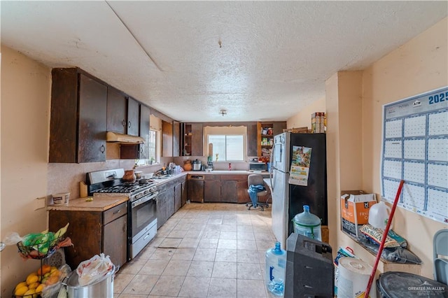 kitchen with a textured ceiling, range hood, appliances with stainless steel finishes, dark brown cabinets, and light tile patterned flooring