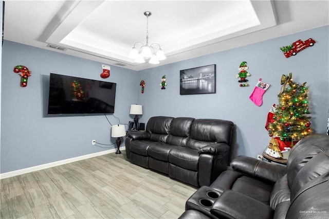 living room featuring a raised ceiling, light hardwood / wood-style flooring, and an inviting chandelier