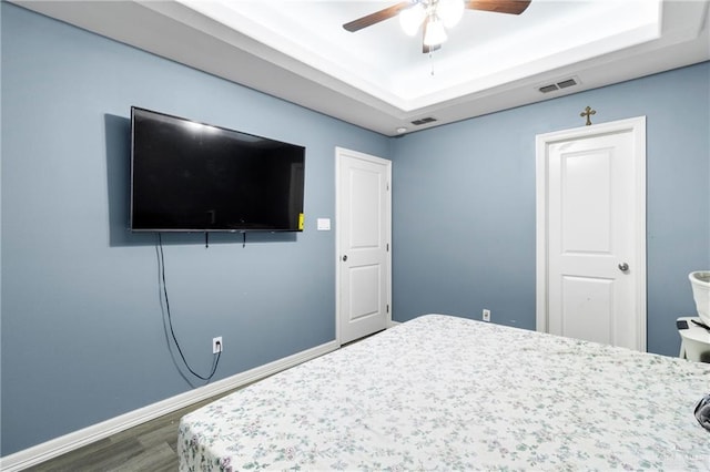 bedroom with dark hardwood / wood-style floors, ceiling fan, and a tray ceiling